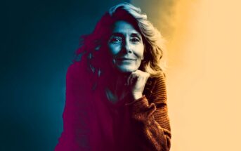 A woman with wavy hair and a warm sweater rests her chin on her hand, smiling softly. The image uses dramatic lighting with blue tones on one side and warm yellow on the other, creating a vivid color contrast.